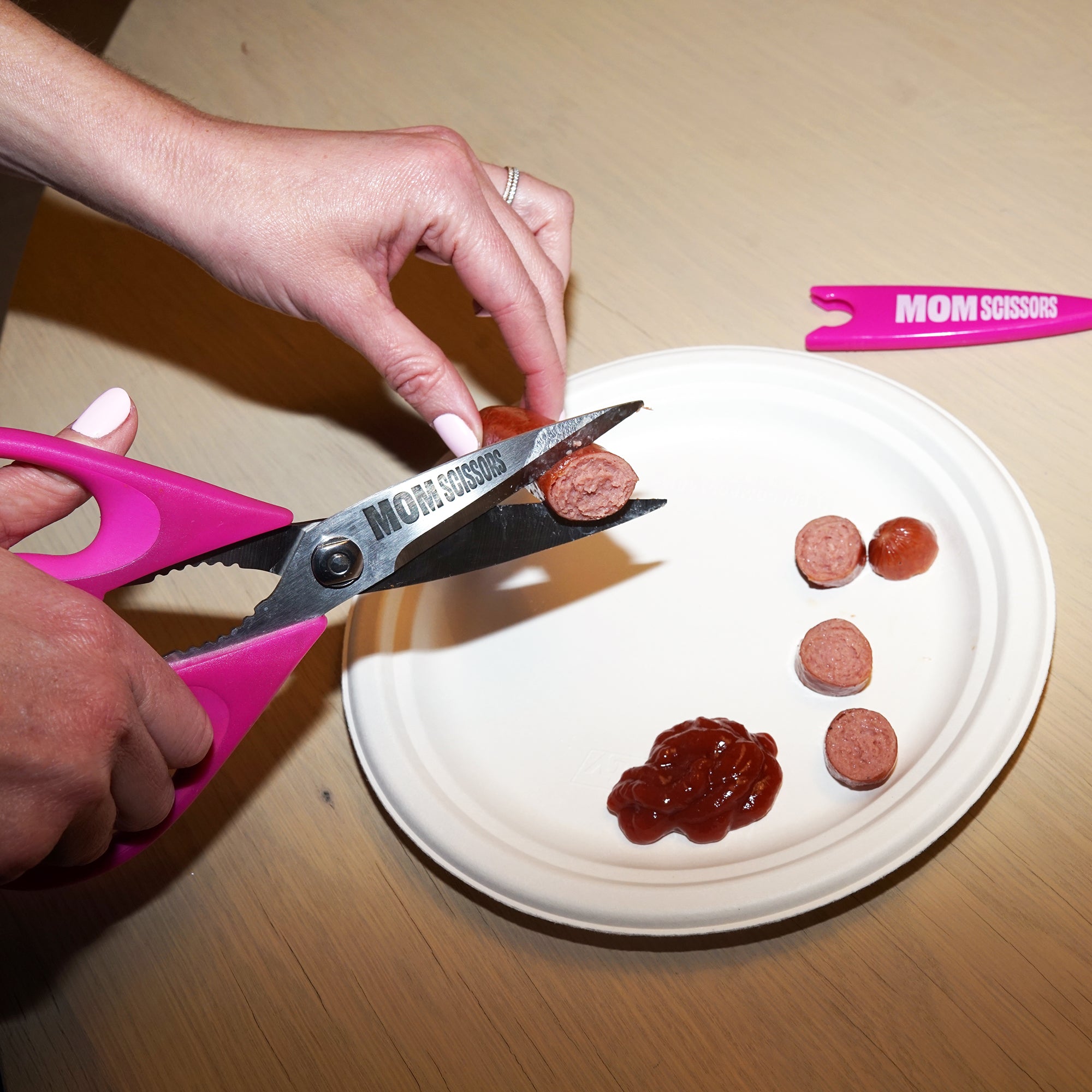 Mom Scissors cutting a hot dog into toddler-sized bites—pink food scissors designed for baby and toddler meals. Perfect as pink baby food scissors or pink food scissors for toddlers, making mealtime quick and easy for parents.