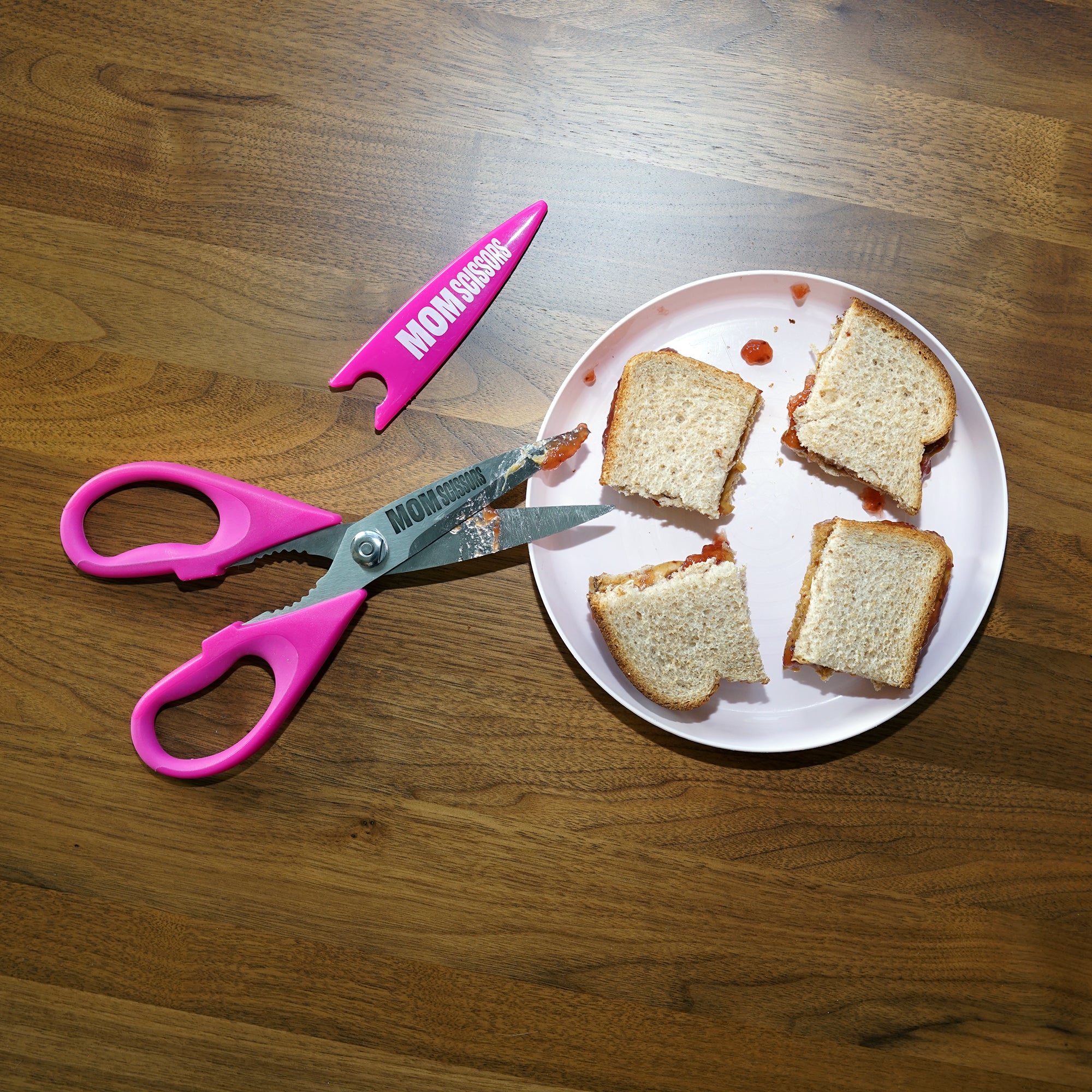 Mom Scissors cutting a peanut butter and jelly sandwich into toddler-friendly portions—pink food scissors designed for toddlers and babies. Perfect as pink baby food scissors or pink food scissors for parents making mealtime easier.